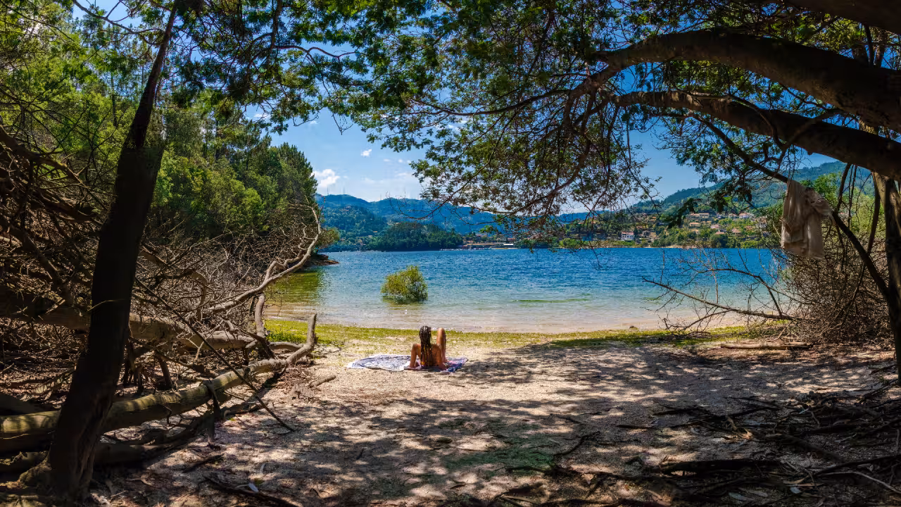 Visitor relaxing on a secluded beach by a serene lake in Peneda Geres National Park, surrounded by lush greenery.