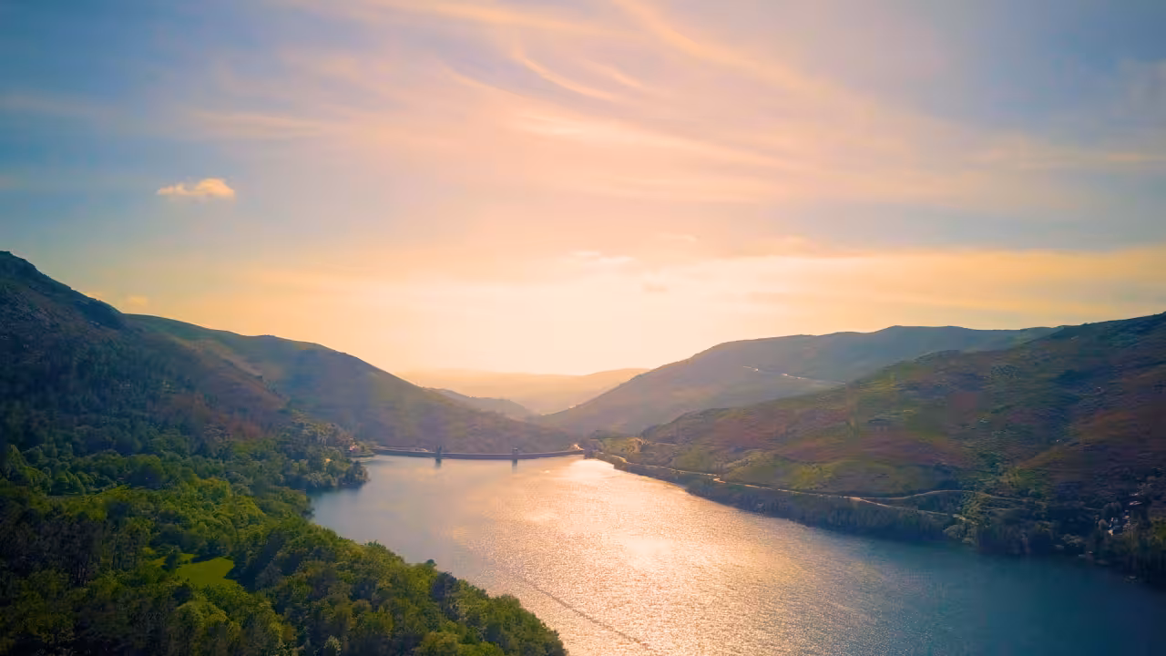 Scenic view of a serene lake surrounded by lush hills under a vibrant sunset in Peneda Geres National Park.