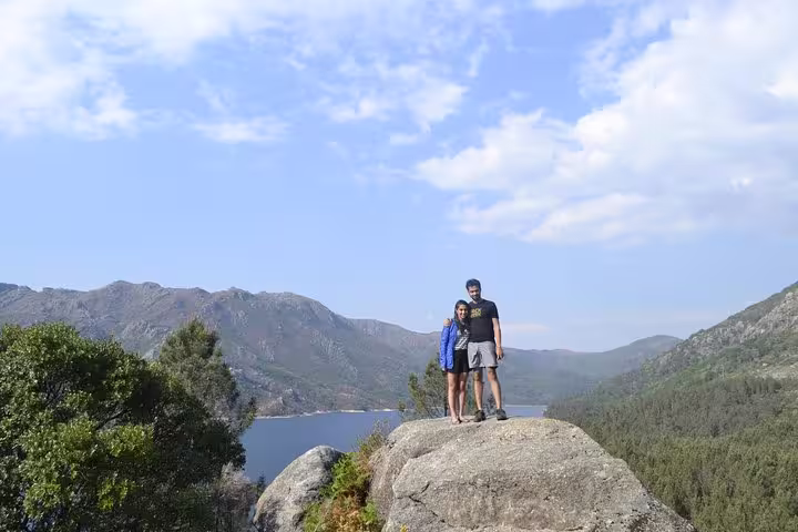 Couple stands on a rock with stunning views of mountains and a lake in Peneda-Gerês National Park under a clear sky.