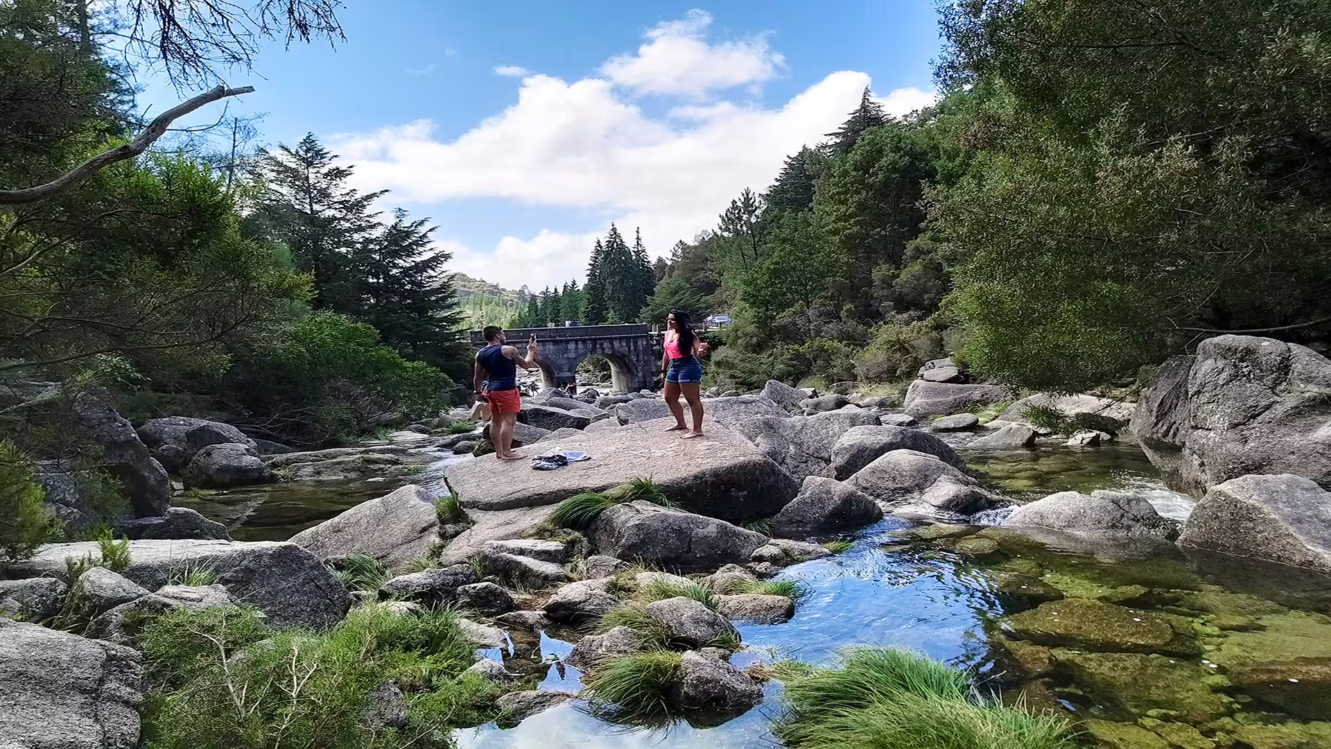 Two people enjoying a picturesque rocky river scene at Peneda-Gerês National Park, ideal for nature lovers and adventure tours.