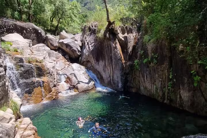 Visitors swimming in a natural rock pool surrounded by lush greenery in Peneda-Gerês National Park.
