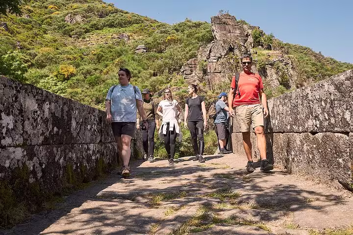 Tour group exploring a scenic stone bridge in Peneda-Gerês National Park under clear blue skies.