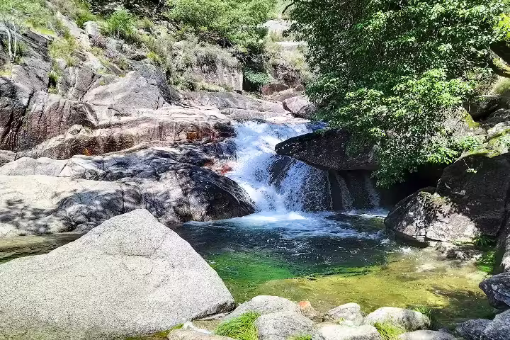Scenic waterfall amidst lush greenery and rocky landscape in Peneda-Gerês National Park, perfect for nature enthusiasts.