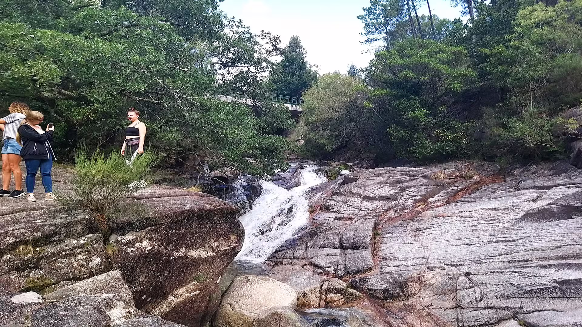 Visitors enjoying a scenic waterfall surrounded by lush greenery and rocky terrain at Peneda-Gerês National Park on a private tour.