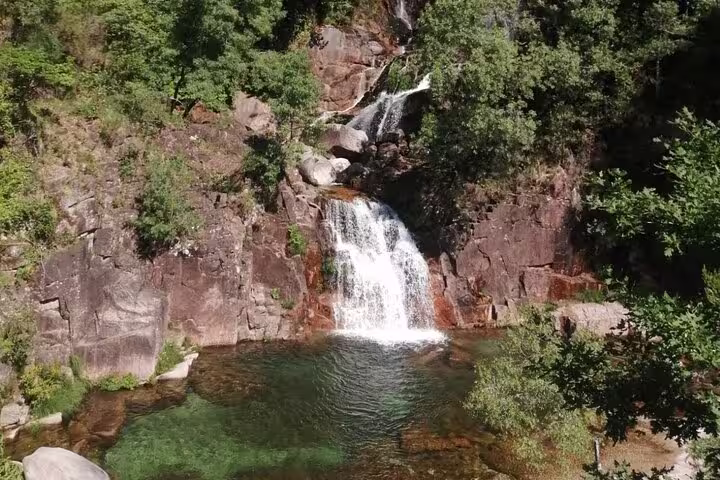 Scenic waterfall cascading into a clear pool surrounded by lush greenery in Peneda Geres National Park.