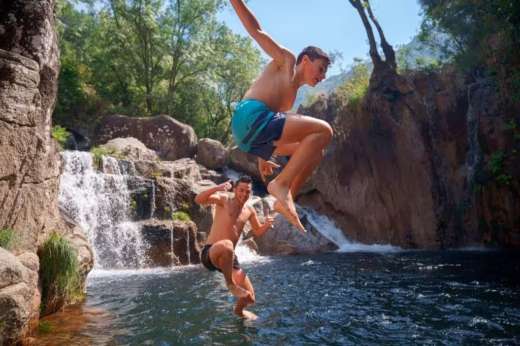 Visitors leap into a refreshing waterfall pool in Peneda-Gerês National Park, ideal for summer adventures.