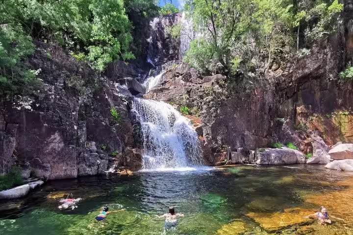 Visitors enjoy swimming beneath a cascading waterfall in Peneda-Gerês National Park, surrounded by lush greenery.