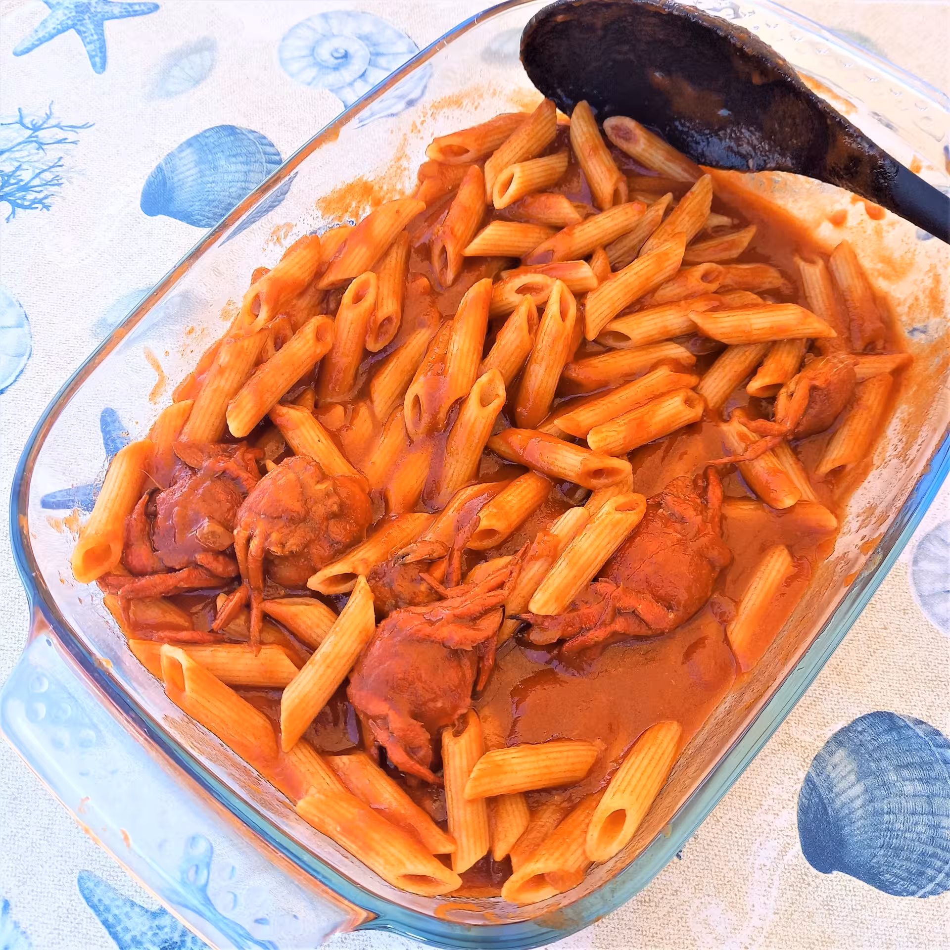 Delicious penne pasta with crab in rich tomato sauce served on a sea-themed tablecloth.