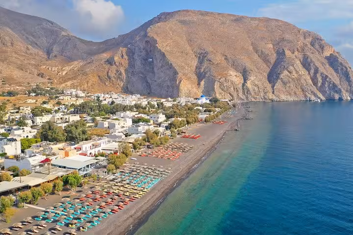 Aerial view of Perissa Beach Santorini with black sand shore and umbrellas on Athens to Santorini private tour