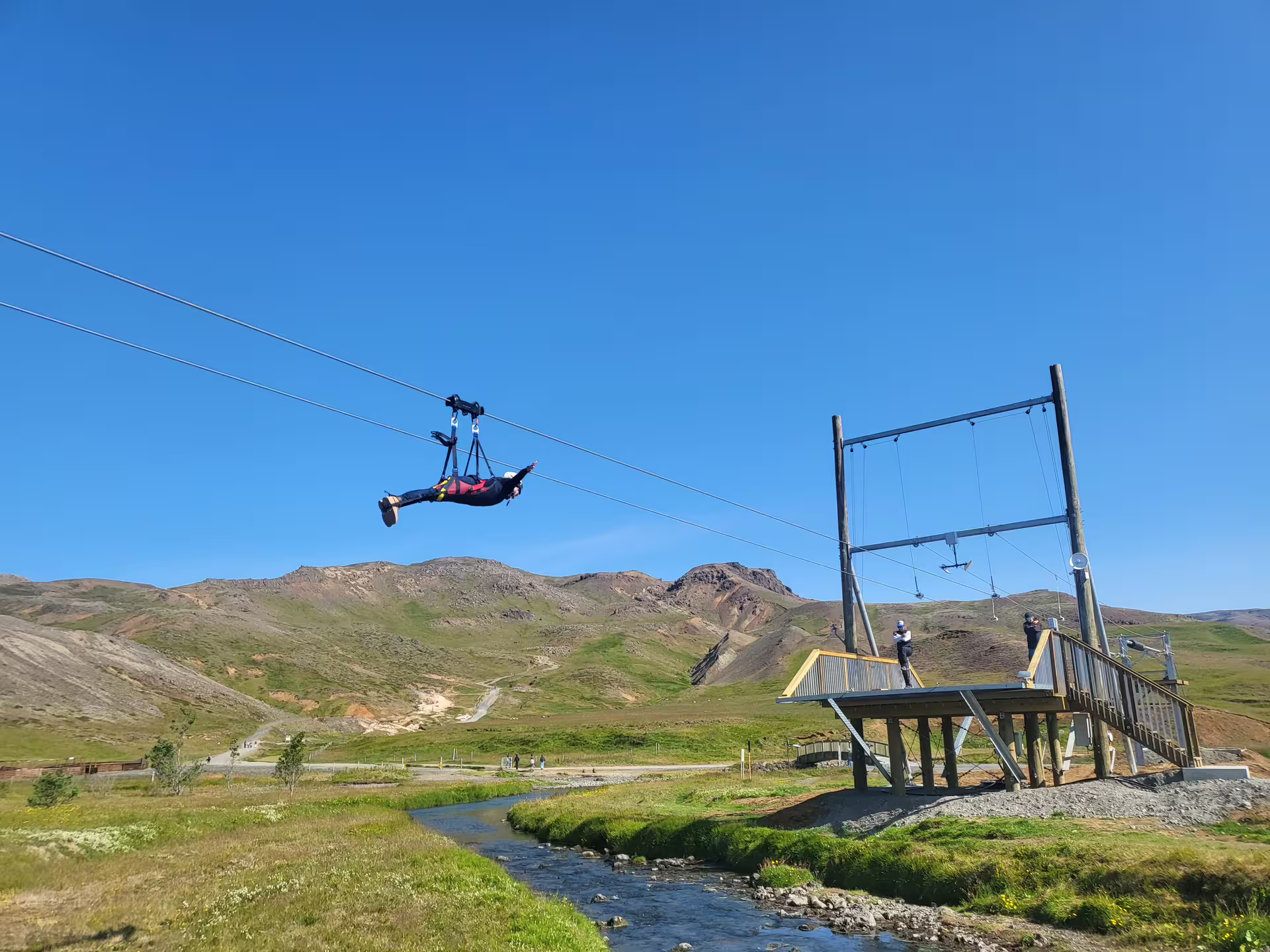 Person ziplining over a scenic valley with a clear blue sky, showcasing adventure and freedom in a stunning landscape.
