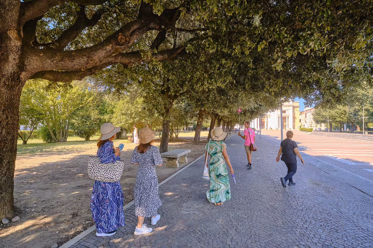 Visitors stroll under shaded trees on a sunny day in Orvieto, perfect for a leisurely exploration of Umbria.