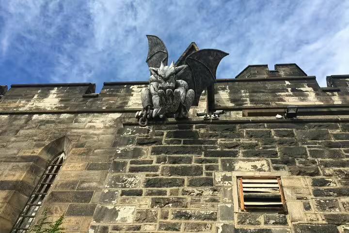 Gothic gargoyle statue with bat wings perched on weathered stone castle wall under blue sky