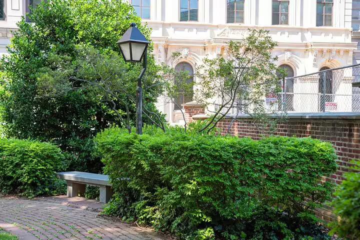 Historic Philadelphia garden with brick path, iron lamp post, wooden bench, and lush green hedges near ornate white building