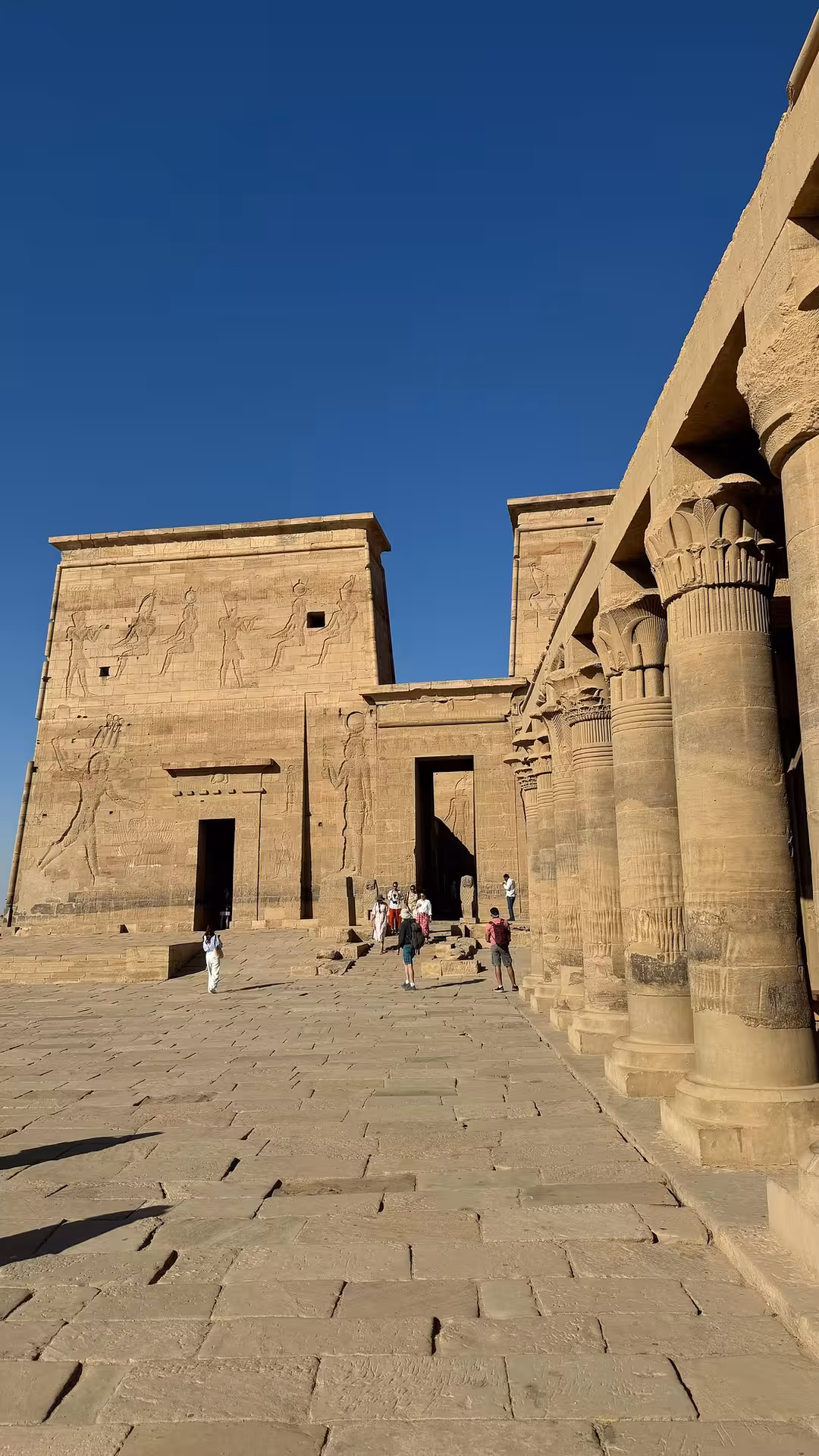 Tourists explore the ancient Philae Temple under a clear blue sky on a multi-day Luxor and Aswan trip, Egypt.