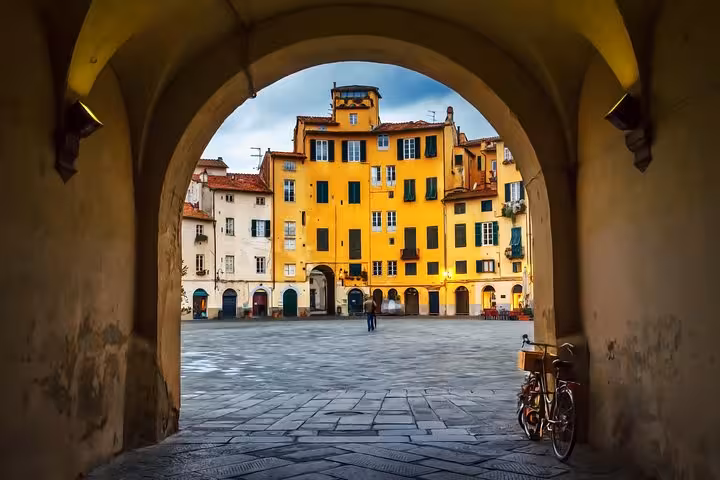 View through an archway of Piazza dell'Anfiteatro in Lucca, Italy, featuring colorful historic buildings and a bicycle.