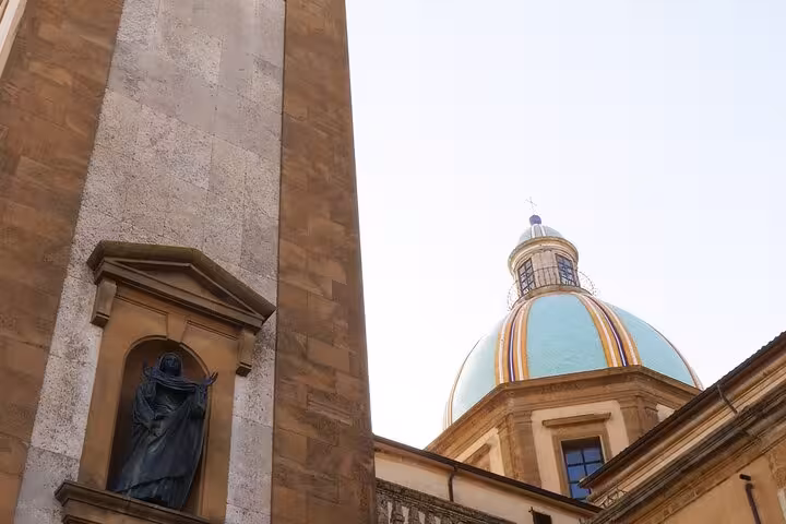 Close-up of a statue and dome in Piazza Armerina, highlighting architectural details and vibrant colors against the sky.