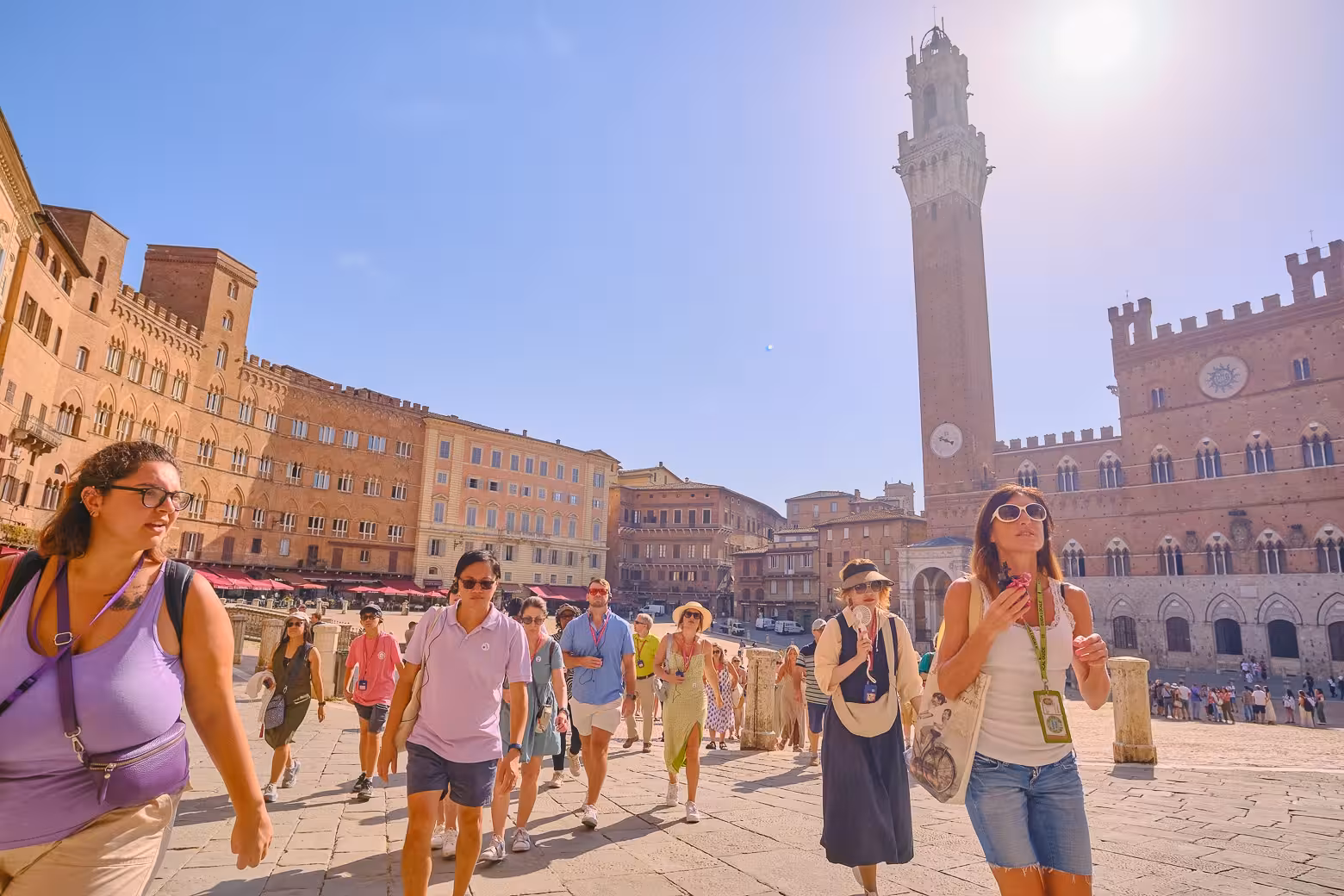 Tourists explore Piazza del Campo in Siena on a sunny day during a Pisa, Siena, and San Gimignano day trip.