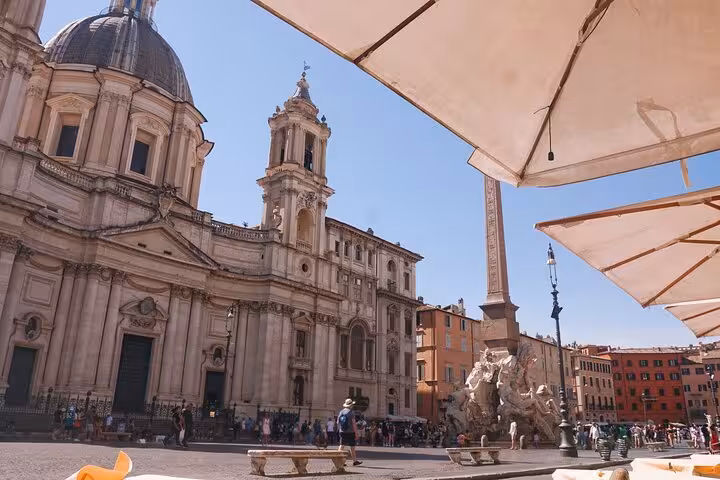 Scenic view of Piazza Navona in Rome featuring historical architecture under sunlit umbrellas.