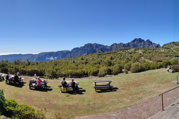 Visitors enjoying a sunny day on picnic benches with panoramic views of Pico do Arieiro's rugged mountainscape.
