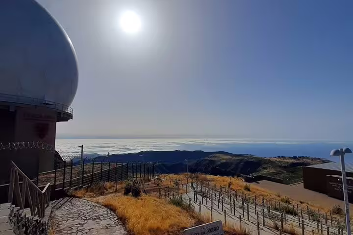 Observatory at Pico Do Arieiro with a bright sun and sweeping views of the ocean and rugged Madeira landscape.