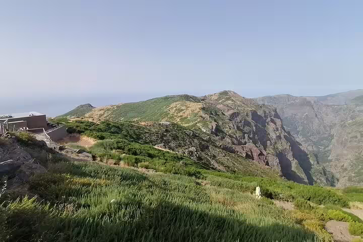Expansive view of Pico do Arieiro's verdant slopes and majestic cliffs under a clear, sunny horizon.