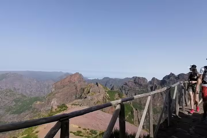 Tourists enjoy a scenic walk along the wooden railing path with panoramic views of Pico do Arieiro's rocky landscape.