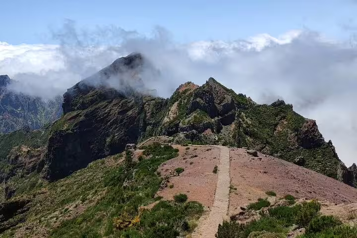 Stunning view of Pico do Arieiro hiking trail with lush greenery and dramatic mountain peaks surrounded by clouds.