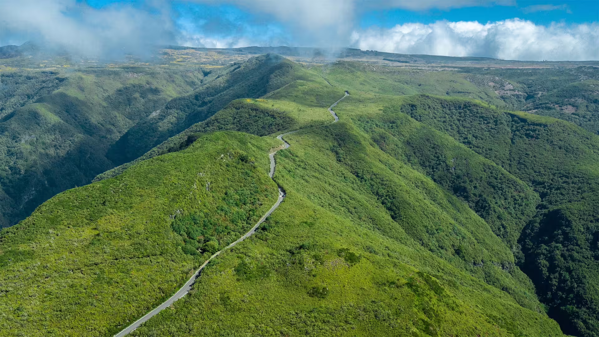 Scenic aerial view of lush green mountains and winding roads on the Pico do Arieiro full-day tour in Madeira.