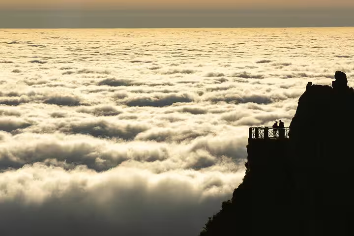 Silhouetted hikers admire stunning cloudscape at sunrise from Pico do Arieiro, Madeira's breathtaking viewpoint.