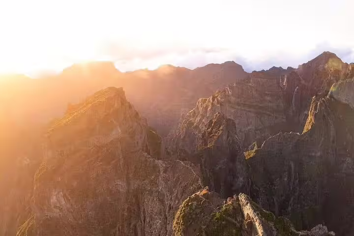 Golden sunrise illuminating the rugged peaks of Pico do Arieiro, creating a dramatic and serene mountain scene.