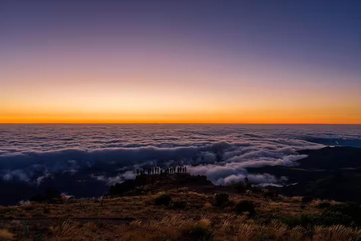 Dawn breaks over Pico do Arieiro, with a vibrant horizon and clouds beneath, perfect for a sunrise hike.