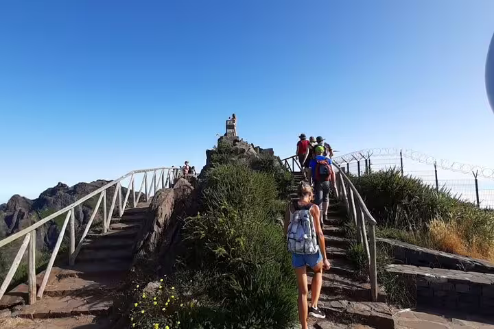 Hikers ascending the scenic trail at Pico Ruivo surrounded by lush greenery and clear blue skies.