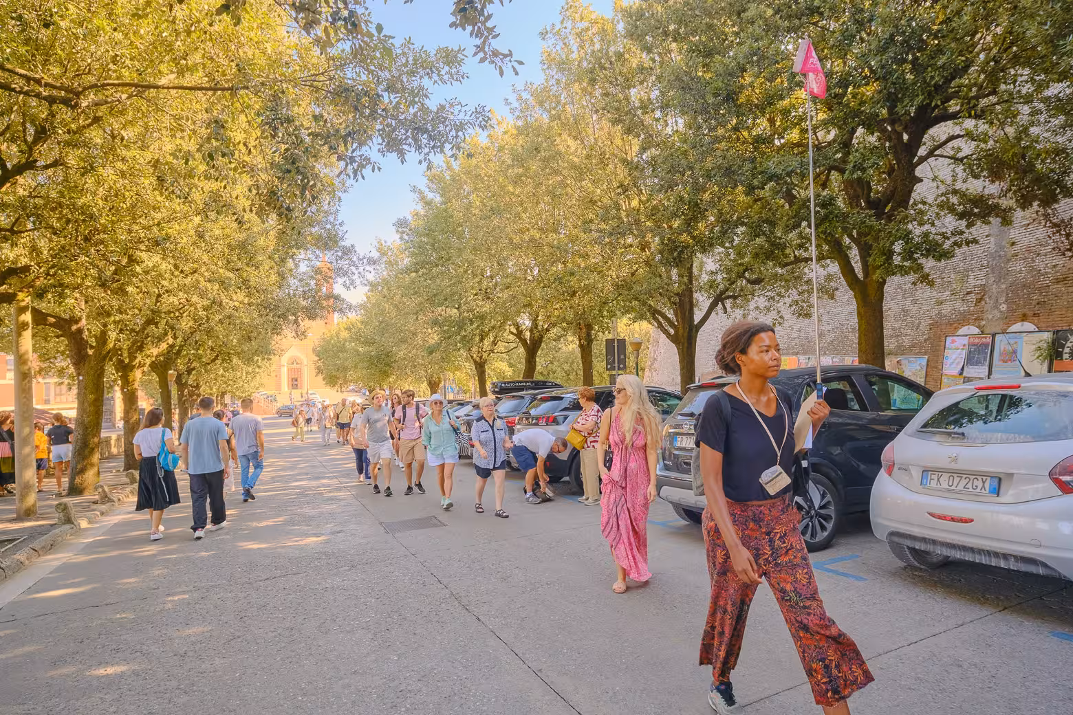Tourists stroll along a shaded street in Pienza, enjoying the Land of Brunello wine tour.