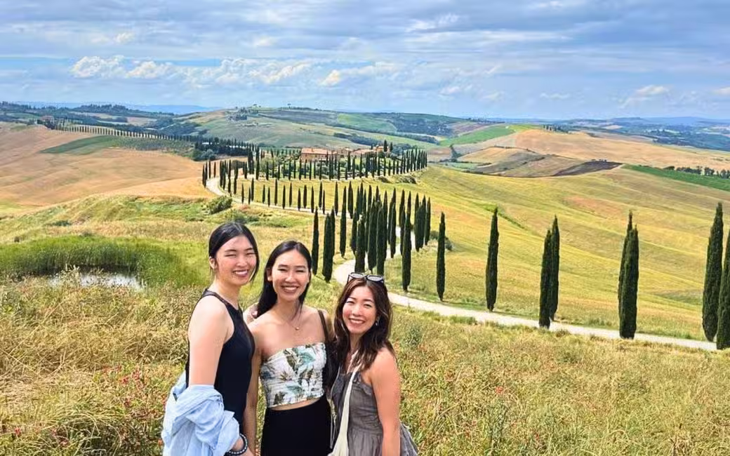 Three visitors smile with the scenic Tuscan countryside of Pienza and Montepulciano as their picturesque backdrop.