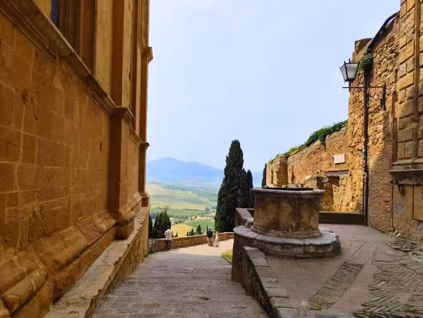 Charming alleyway in Pienza with stone architecture and scenic countryside views in the distance.