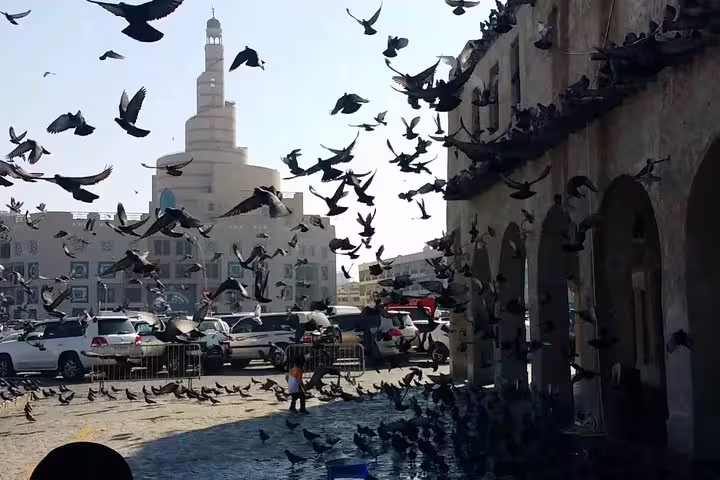Flock of pigeons in motion at Souq Waqif with iconic spiral tower in background on Doha Transit City Tour.