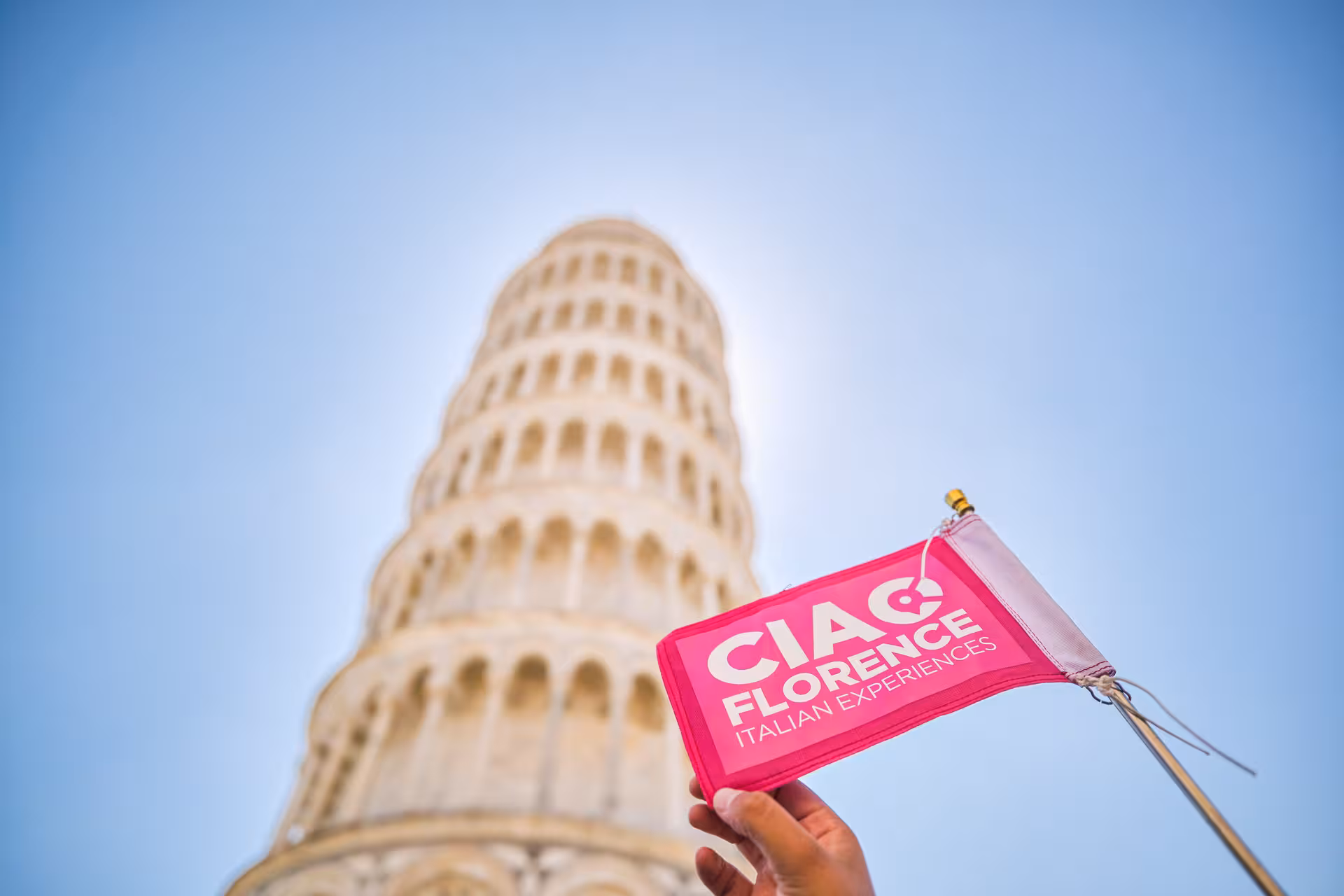 Hand holding a pink flag in front of the Leaning Tower of Pisa during a Florence and Pisa shore excursion from Livorno.