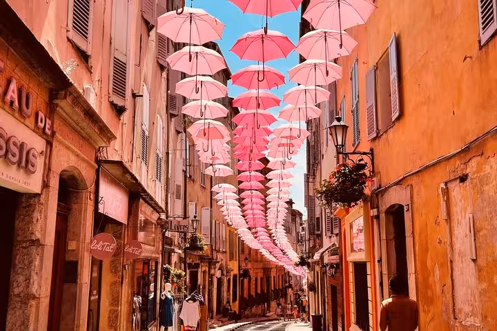Charming street adorned with hanging pink umbrellas in a vibrant village on a private tour of local sights.