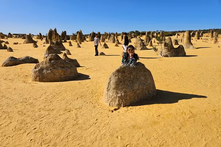 A visitor poses on a limestone formation in the Pinnacles Desert, capturing the essence of Pinnacle Day Adventure Tour.