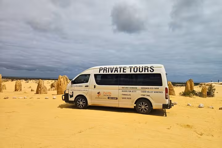Private tour van parked among the iconic Pinnacles Desert formations, showcasing the Pinnacle Day Adventure Tour experience.