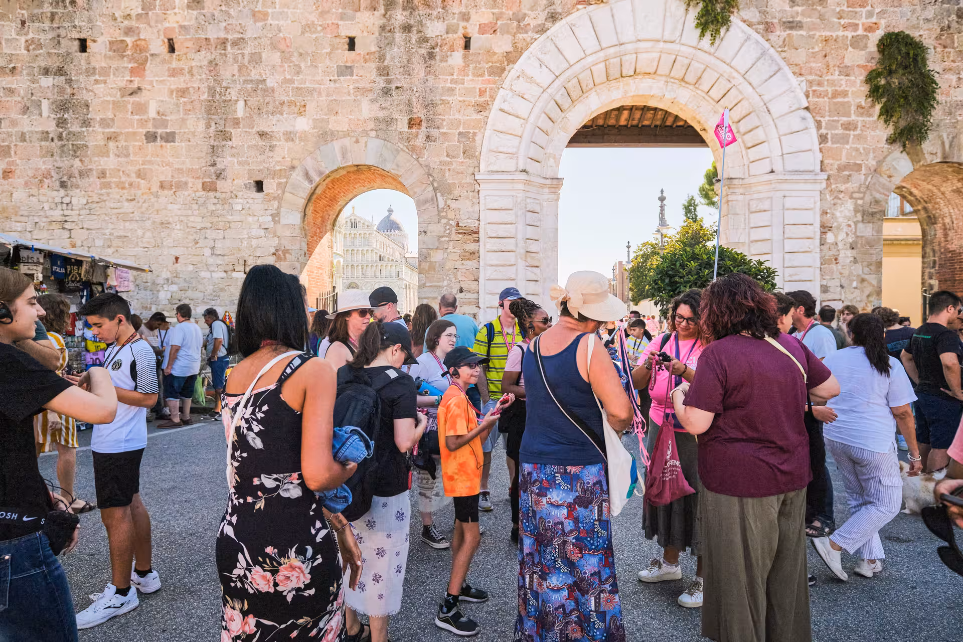 Crowds of tourists gather near Pisa’s historic archway, with the iconic cathedral visible in the background.