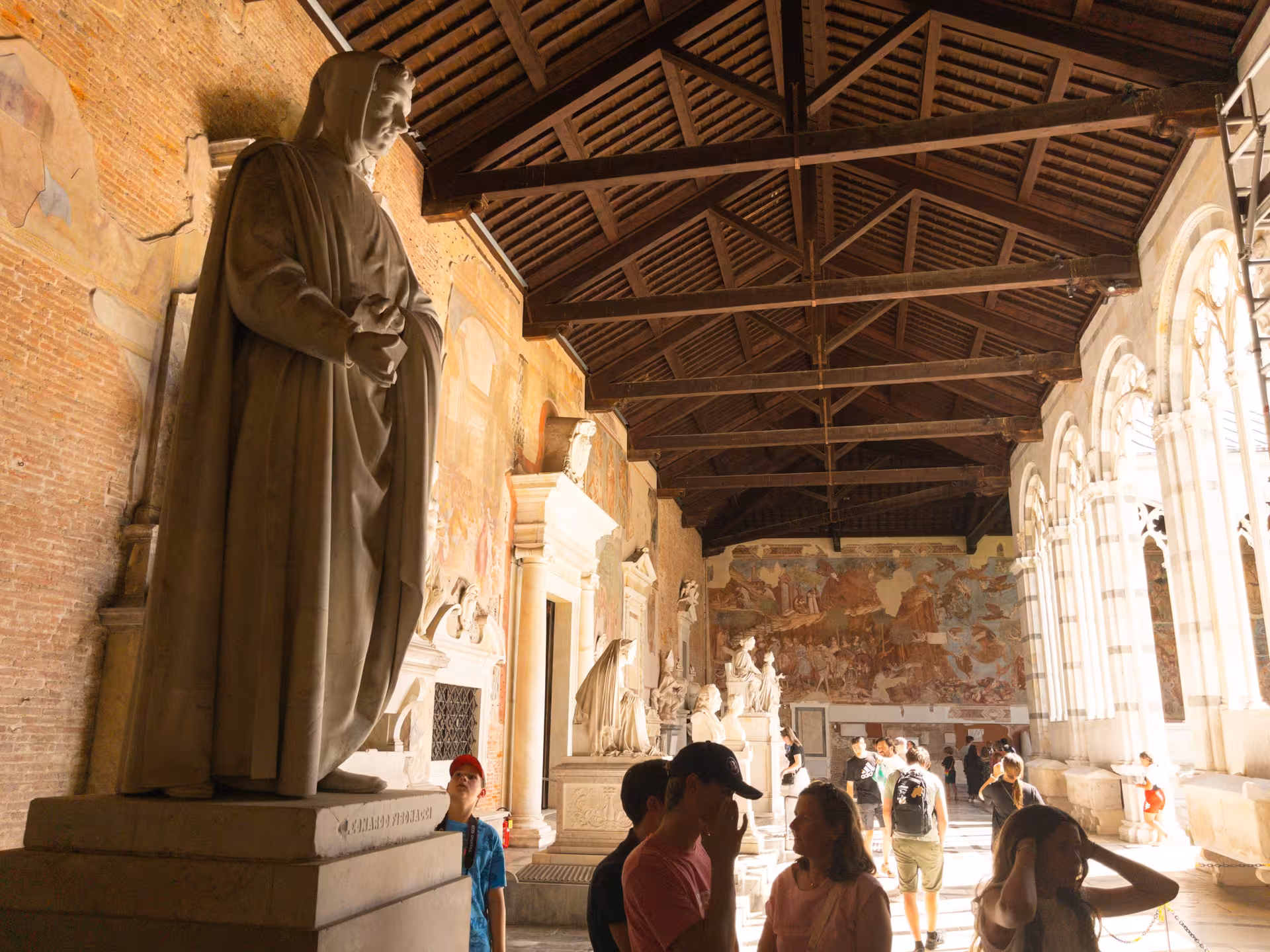 Visitors explore historic frescoed corridor with statues in Pisa, a highlight of the Florence to Pisa day tour.