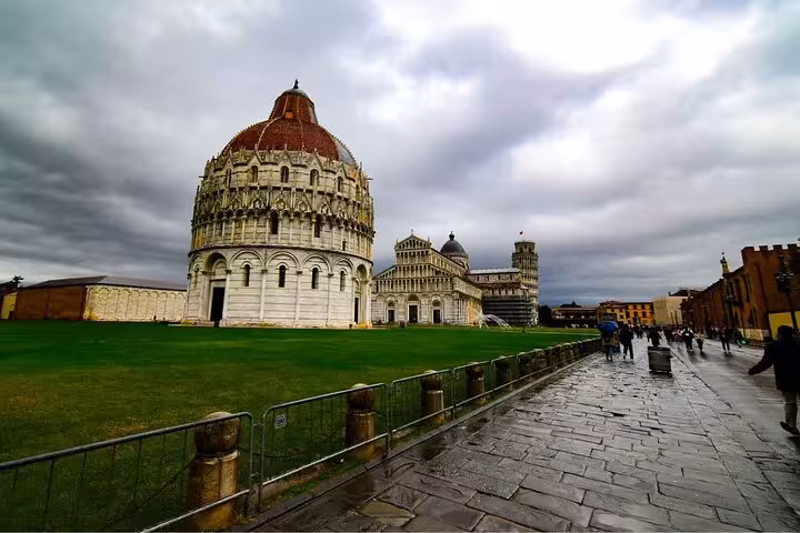 Dramatic view of Pisa's Baptistery and Leaning Tower under a cloudy sky on a day tour from Rome.