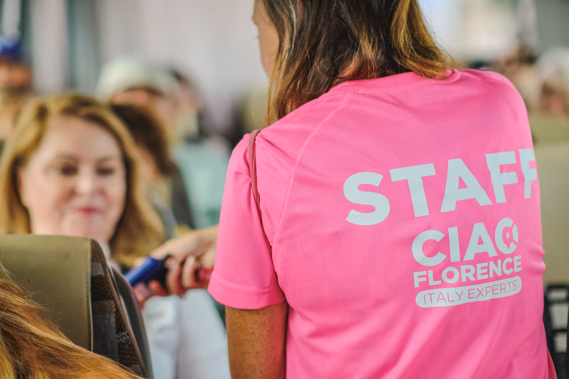 Friendly staff in pink shirts assisting travelers on the Pisa and Lucca day trip from Florence, ensuring a smooth experience.