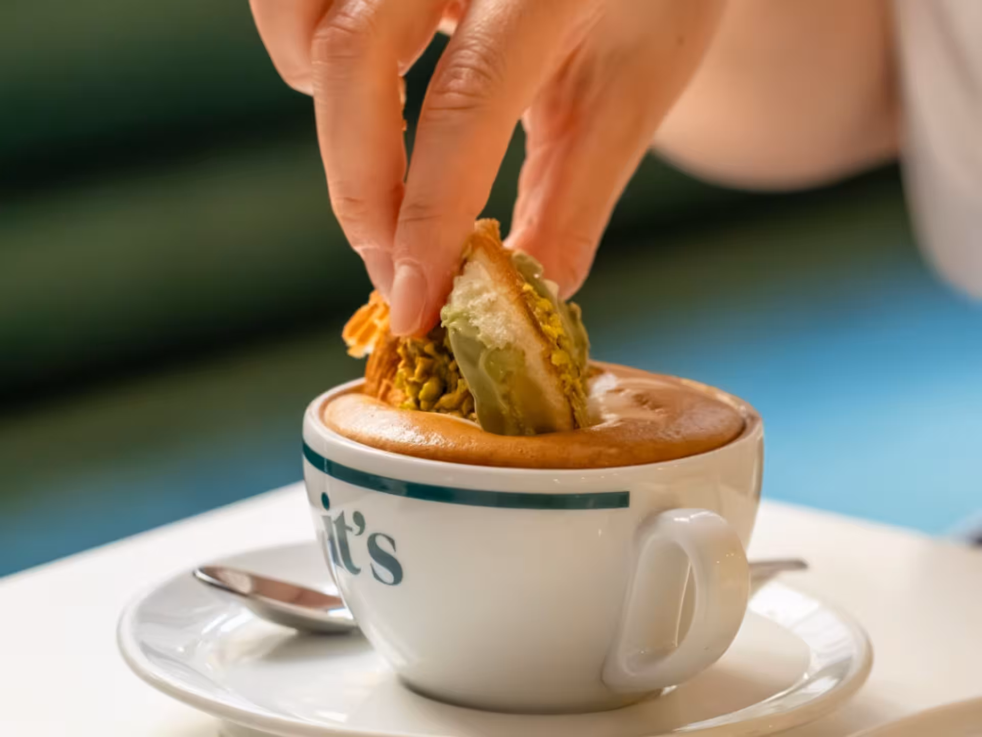 Hand dipping a pistachio pastry into a rich Neapolitan cappuccino.