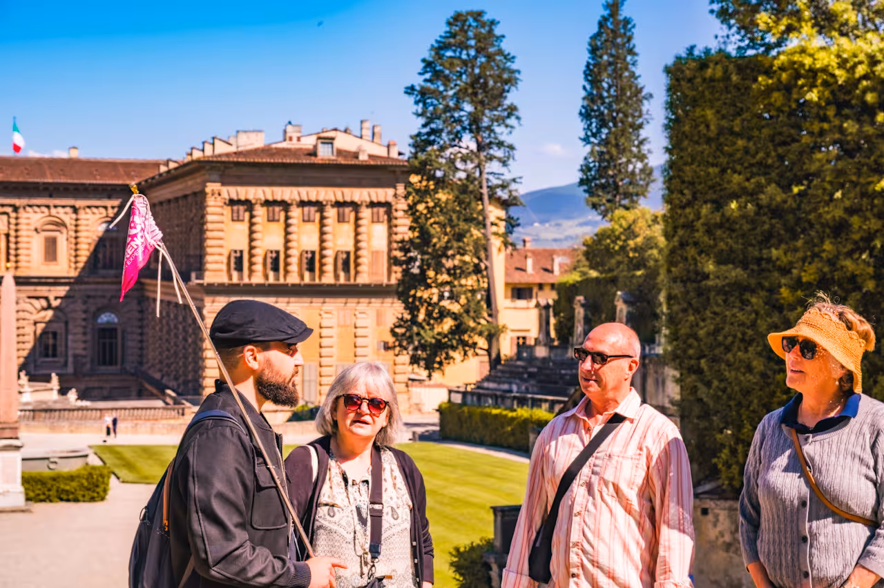 Visitors enjoying a guided tour at Pitti Palace with lush gardens in the background on a sunny day.