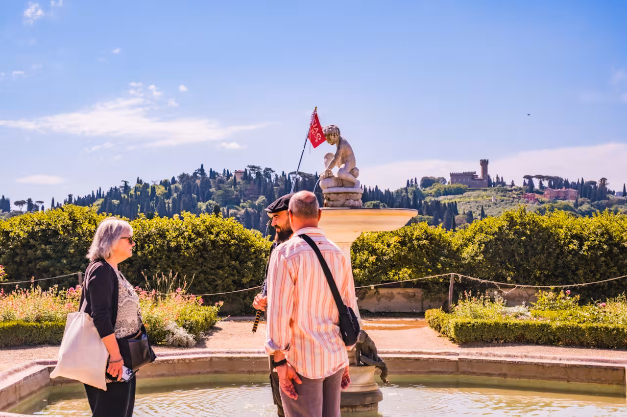 Visitors discussing near a statue in Boboli Gardens with scenic Tuscan hills in the background.