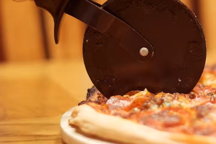 Close-up of a pizza cutter slicing through a freshly baked pizza, highlighting the culinary experience in Florence.