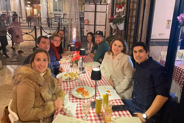 Group enjoying a meal at a cozy outdoor restaurant in Rome's Piazza Navona during a pizza and tiramisu cooking class.