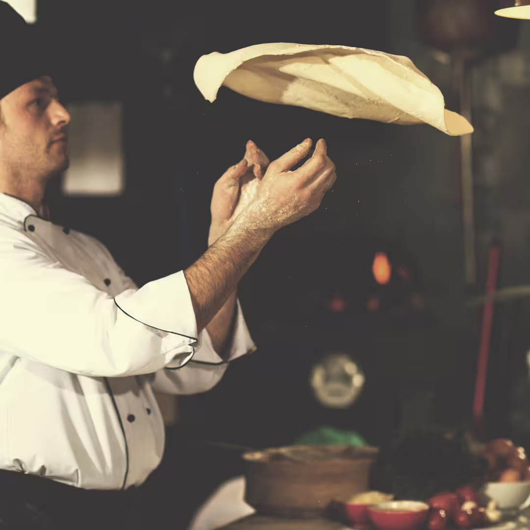 Pizzaiolo tossing pizza dough high in a traditional wood-fired kitchen during immersive Naples pizza making master class